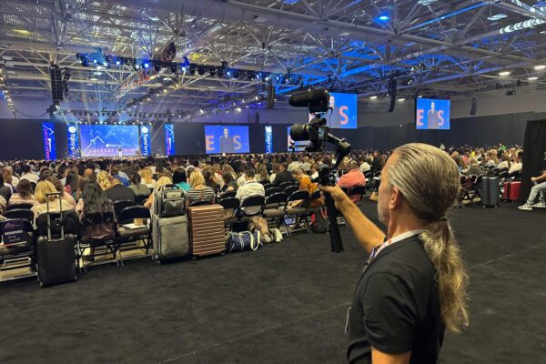 Camera operator filming a keynote from the back of a large conference hall