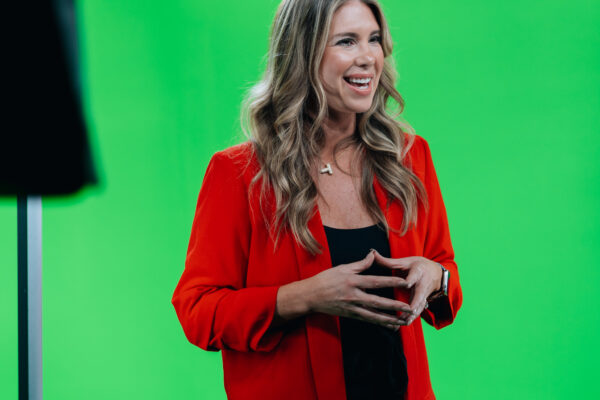 Woman in a red blazer speaking on the green screen stage